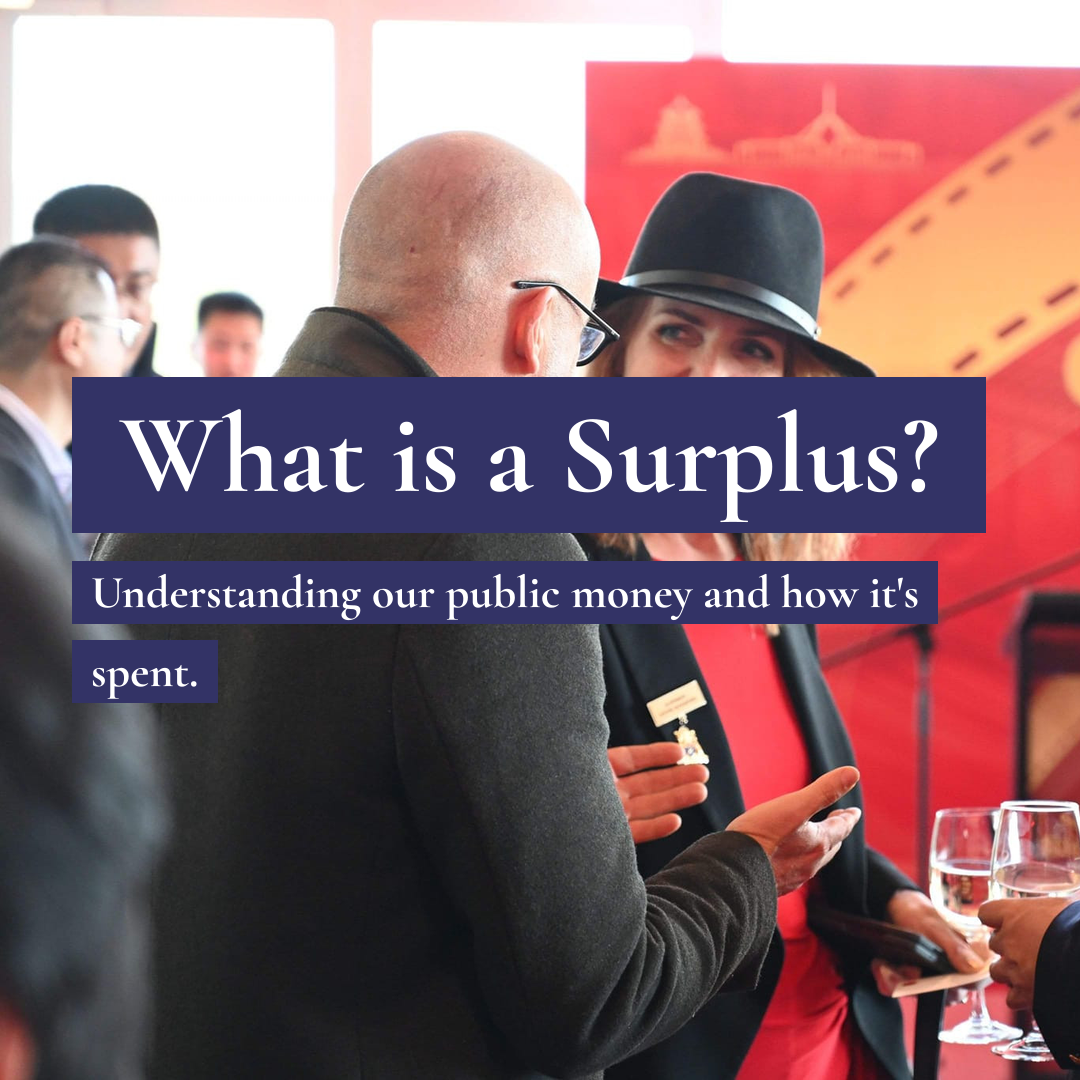 A man and woman talk at an event with text: What is a Surplus? Understanding our public money and how it's spent.